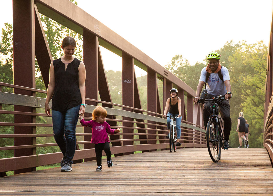 Family walking and cycling on a wooden bridge on the Linear Path